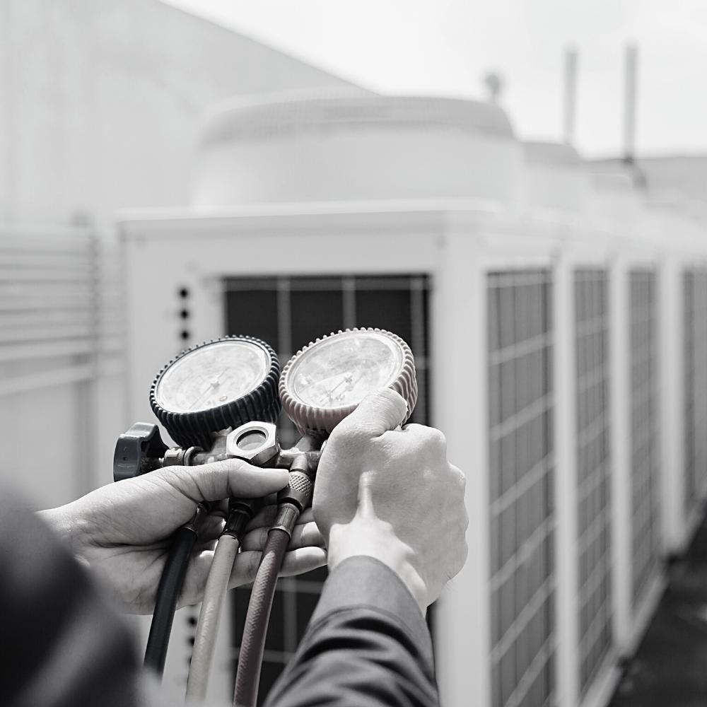 A person performing an air conditioner installation holds two units in a black and white photo.